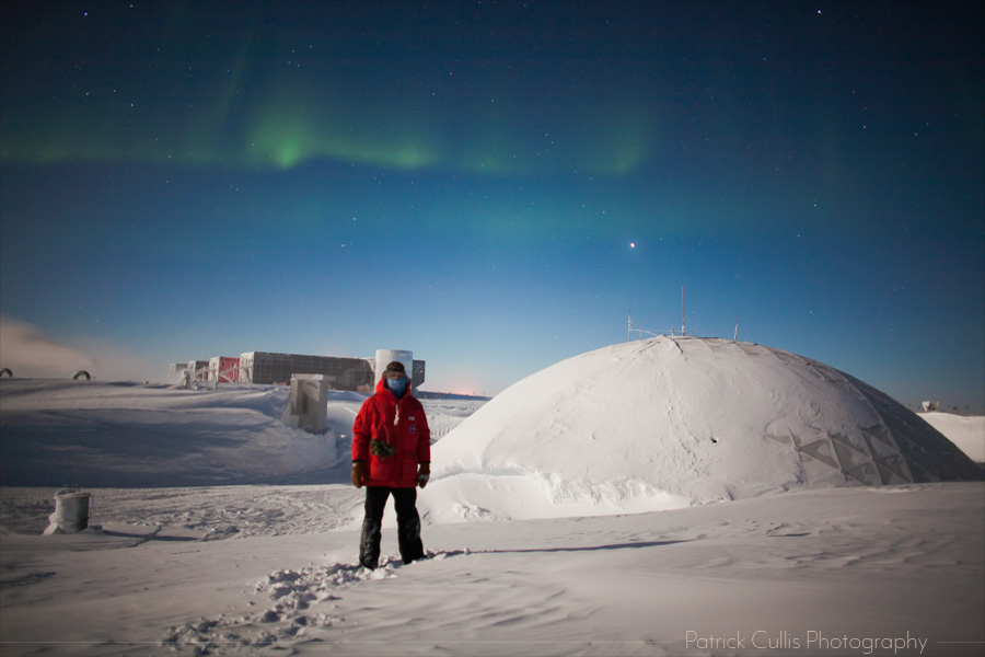 Patrick Cullis posing in front of the Dome and Elevated Stations at the South Pole, Antarctica.